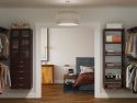 A neatly organized bedroom viewed through an open door, featuring a bed, nightstand, lamp, and adjacent open closet with John Louis Home solid wood storage towers with and shelves full of shoes and clothes.