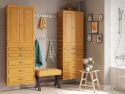 A tidy and coordinated bathroom interior featuring John Louis Home solid wood storage towers a wooden bench with a yellow cushion, and decorative items on a small table, like a potted plant and books.
