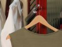 A close-up of an olive green dress on a wooden hanger, displayed on a John Louis Home valet rod attached to a solid wood storage tower with fluted glass doors to help you stay organized with your clothes