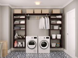 A beautiful well-organized laundry room with white washing machines, a John Louis Home solid wood laundry organizer system with shelving full of baskets, neatly folded linens, various cleaning supplies, and hanging clothes.