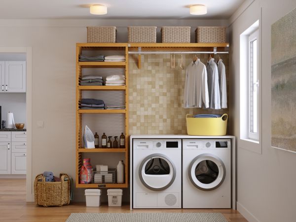 A tidy laundry room with a John Louis Home laundry organizer system with shelving, baskets on top, neatly folded linens, hanging clothes, and front-loading washer and dryer. a yellow basin sits atop the dryer with a kitchen hallway in the right background