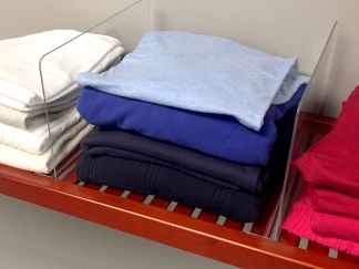 Stacks of neatly folded clothing in various colors organized by a clear John Louis Home shelf divider on a solid wood ventilated shelf.