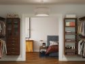 A neatly organized bedroom viewed through an open door, featuring a bed, nightstand, lamp, and adjacent open closet with John Louis Home solid wood storage towers and shelves full of shoes and clothes.